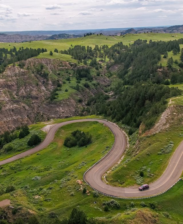 Aerial view of a car on a road winding through the badlands of Makoshika State Park