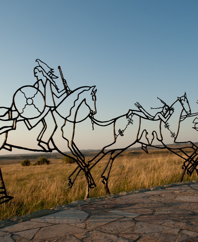 An outline of 3 warriors and a woman riding 3 horses in a line The Indian Memorial at the Little Bighorn Battlefield