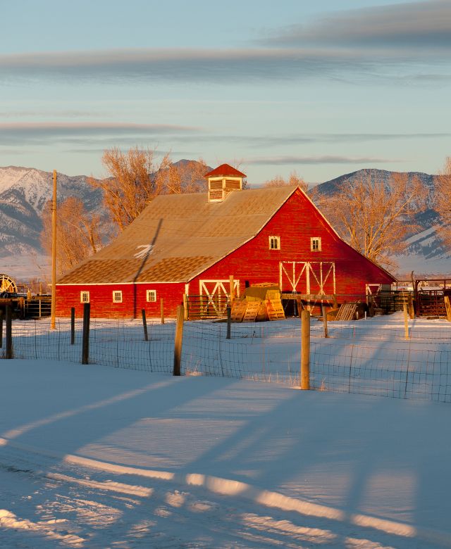 A large red barn against snow covered hills