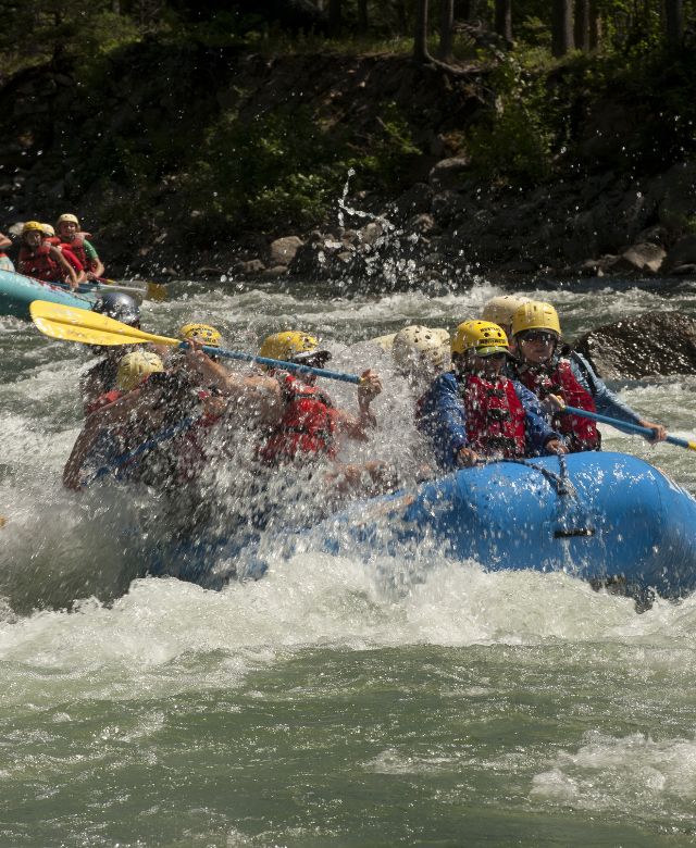 A group of people in a rubber raft riding the whitewater of Gallatin River