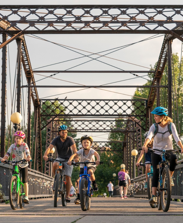 Family of four riding bikes across Van Buren Foot Bridge over the Clark Fort River in Missoula Montana