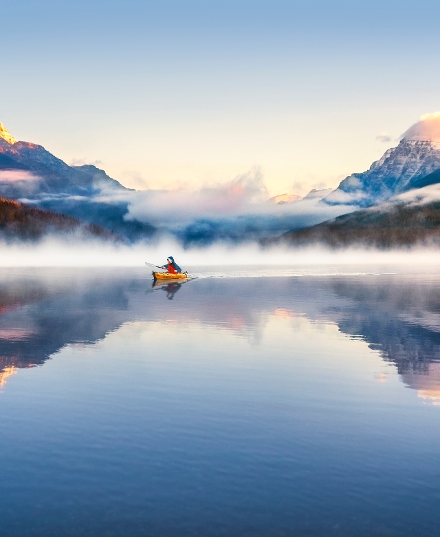 Kayaker on a fog-shrouded Bowman Lake with snow peaked mountains in the background