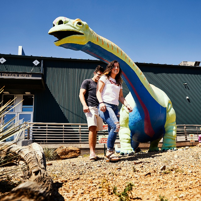 A couple standing under a dinosaur sculpture at the Great Plains Dinosaur Museum and Field Station