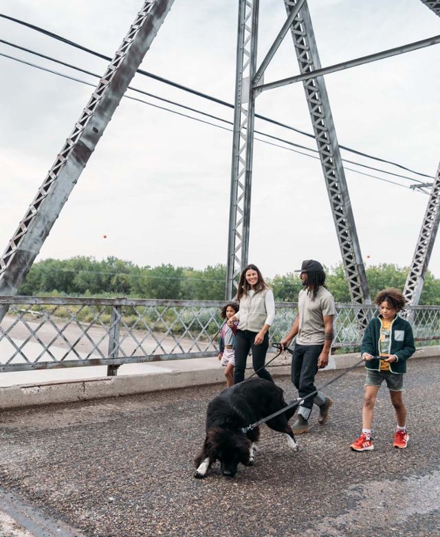 Family of four and their dog walking across an old truss bridge